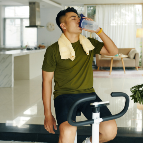 Man on a stationary bike taking a break to drink water in a modern kitchen.