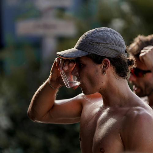 Man drinking from a clear plastic cup outdoors with a blurred background
